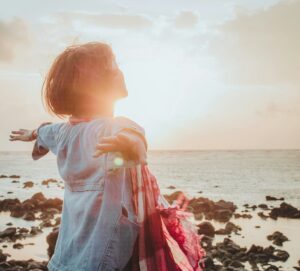une femme debout les bras grands ouverts face à la mer